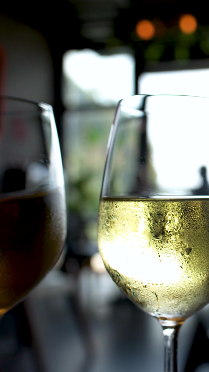 Primo piano di un bicchiere di vino bianco freddo con condensa su un tavolo da patio di un ristorante all'aperto.