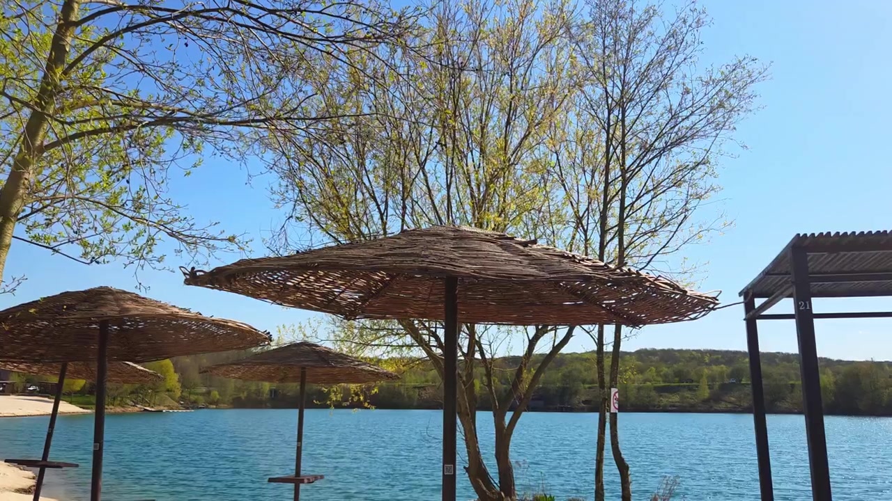 Ombrelloni di paglia su una spiaggia deserta vicino a un lago azzurro e tranquillo sotto un cielo sereno.