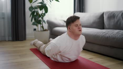 portrait of a guy with down syndrome doing home workouts on the floor, bending back on mat