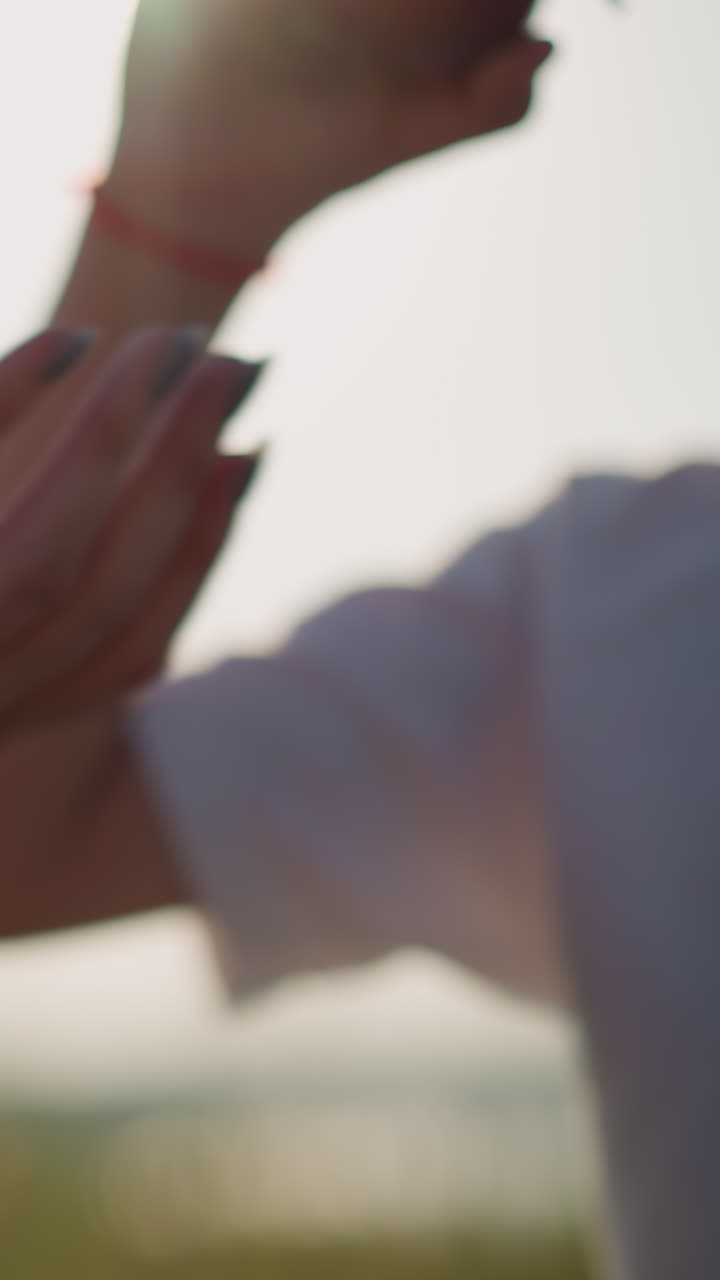 Close-up of a woman's hands carefully cleaning a red apple before handing it to a child wearing a white shirt and glasses. The scene is set outdoors with a bright, natural background