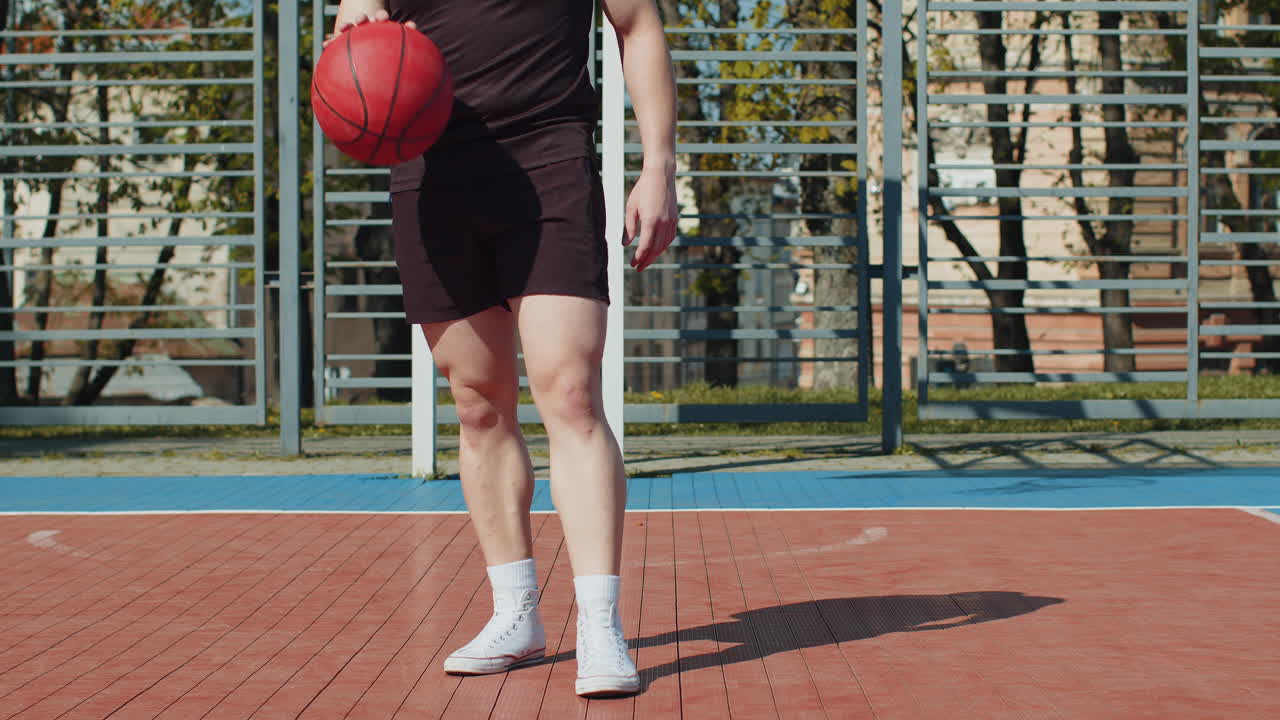 Athletic lebanese man in sportswear playing basketball game dribbling kicks ball on urban city court