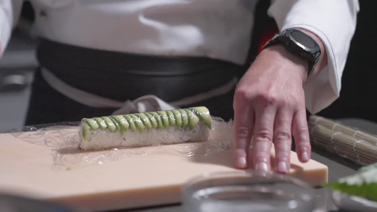 A static shot captures a sushi chef slicing a roll into precise pieces, showcasing expert technique and craftsmanship. Perfect for culinary, sushi preparation, and professional kitchen content.