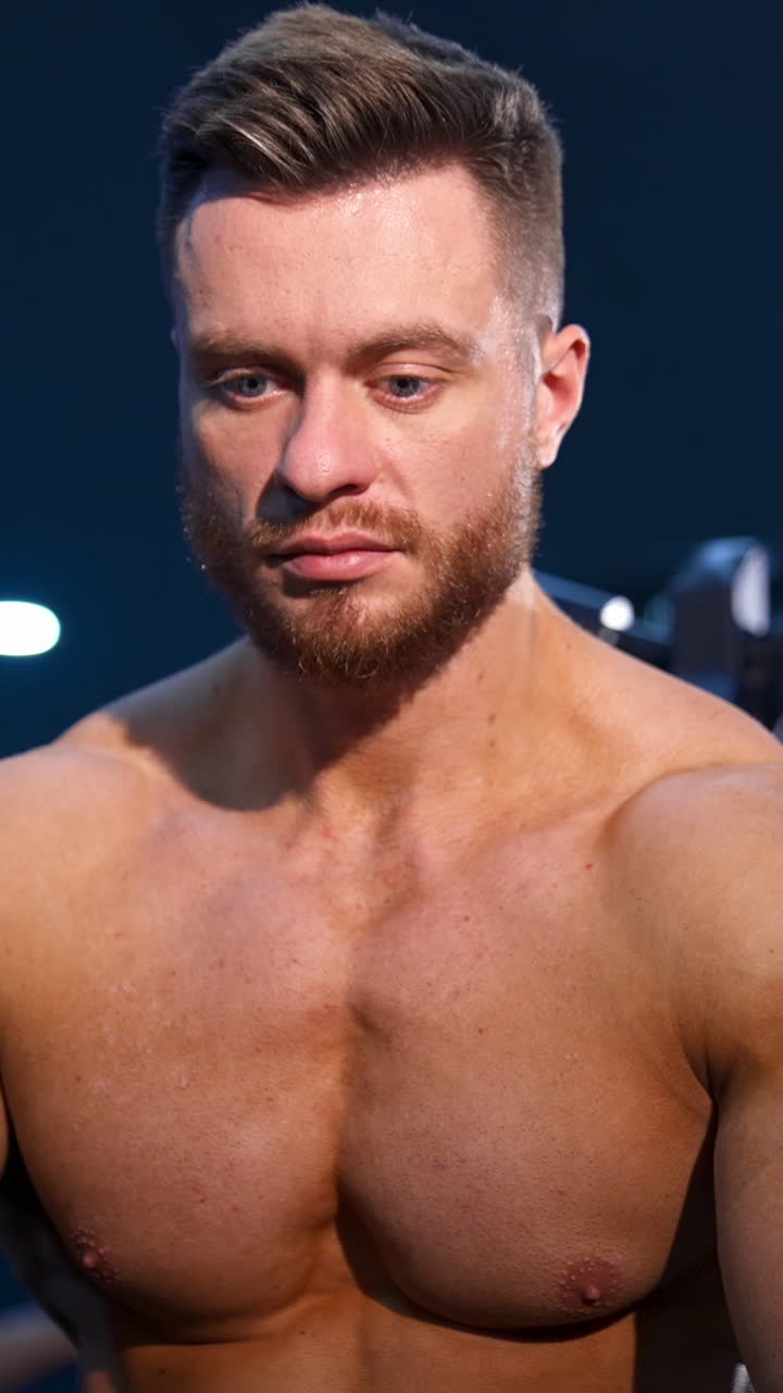 Handsome man with big muscles, posing at the camera in the gym. Modern sport equipment background. Serious bodybuilder. Vertical video
