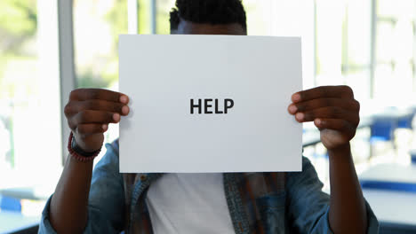 Schoolboy-holding-placard-with-text-help-in-classroom