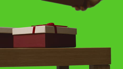 Close-Up-Of-Man-Picking-Up-Gift-Wrapped-Presents-From-Table-Shot-Against-Green-Screen