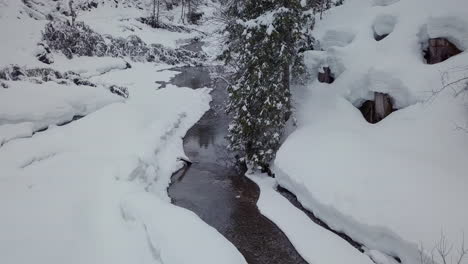 drone flying over a creek in a small snowy valley in the alps