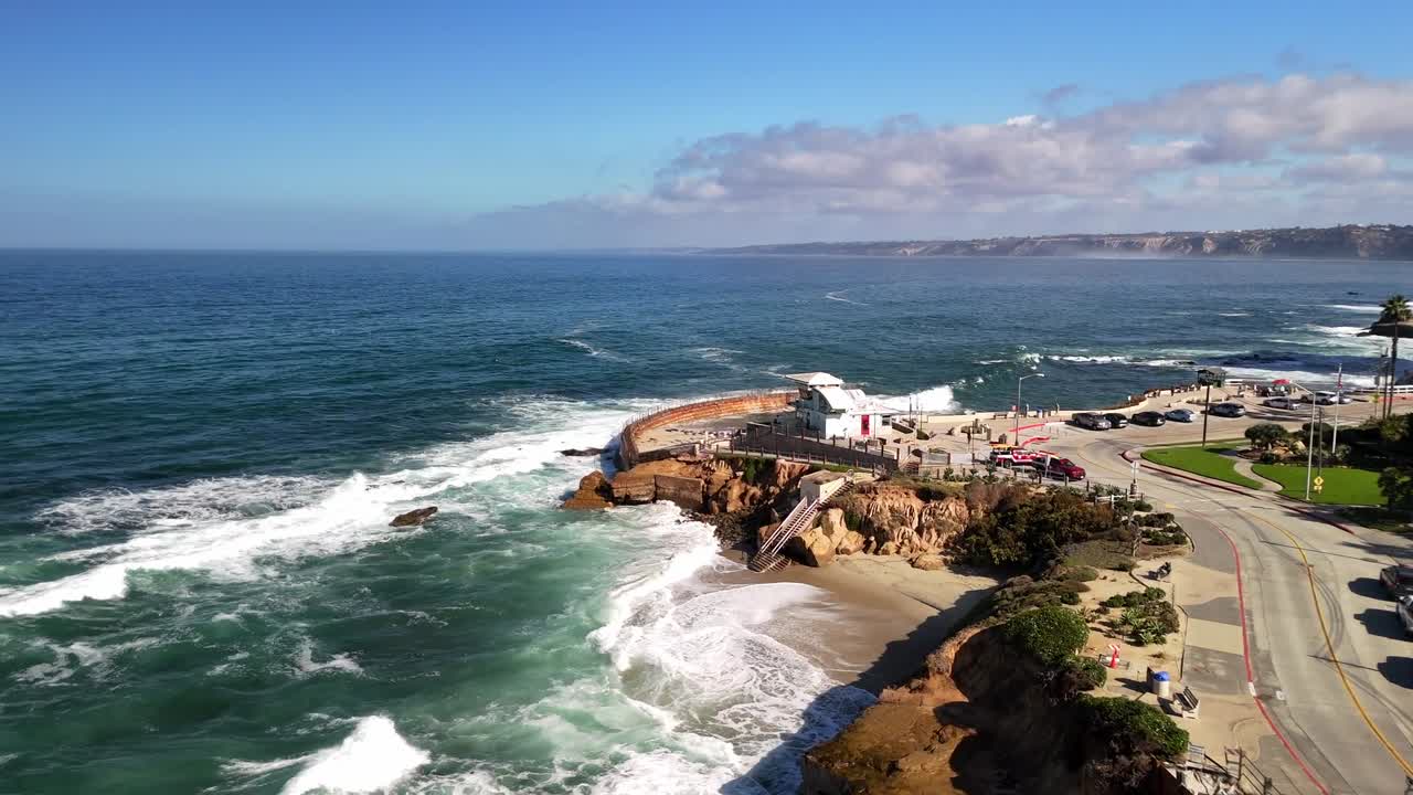 A bright, crisp aerial pass featuring blue water, huge waves, children's pool, and coastline structures