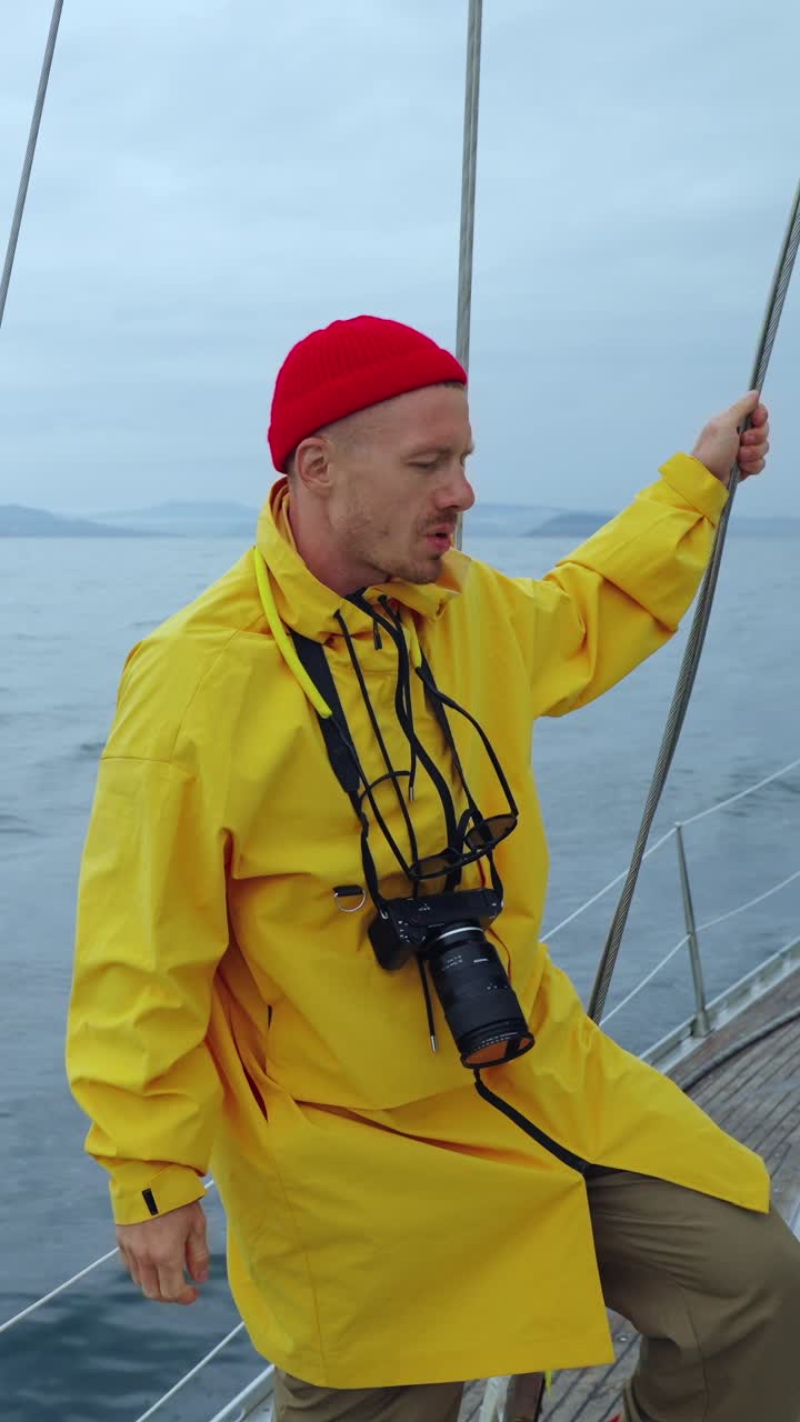 Mann in gelbem Regenmantel und roter Mütze segelt auf dem Ozean