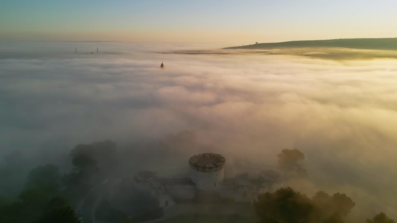 Epic view if a church tower protruding through low hanging clouds during sunrise 4k drone shot video. Drone is slowly flying above a church tower that is only partially visible, sunrise, golden hour
