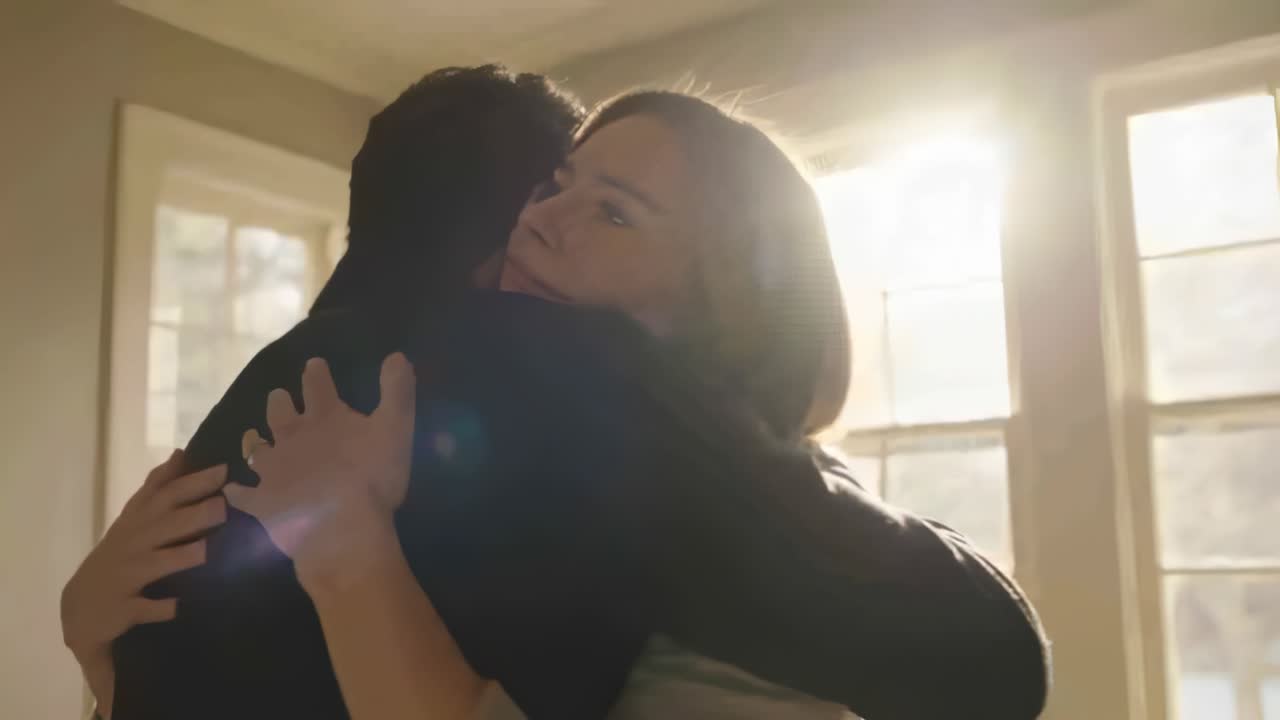Pareja abrazándose buscando alivio en casa frente a una gran ventana que muestra un anillo, con destello de lente.
