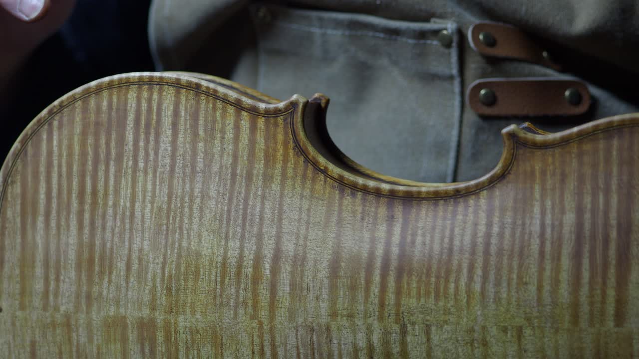 Luthier applying varnish with brush on a violin, skillfully use the finger to spread and enhance the instrument's appearance with an antiquing technique, creating a beautifully aged finish