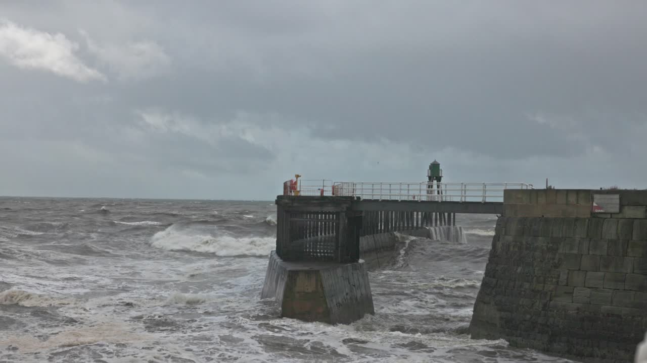 Static shot of waves crashing against the Whitby Harbour walkway during a storm