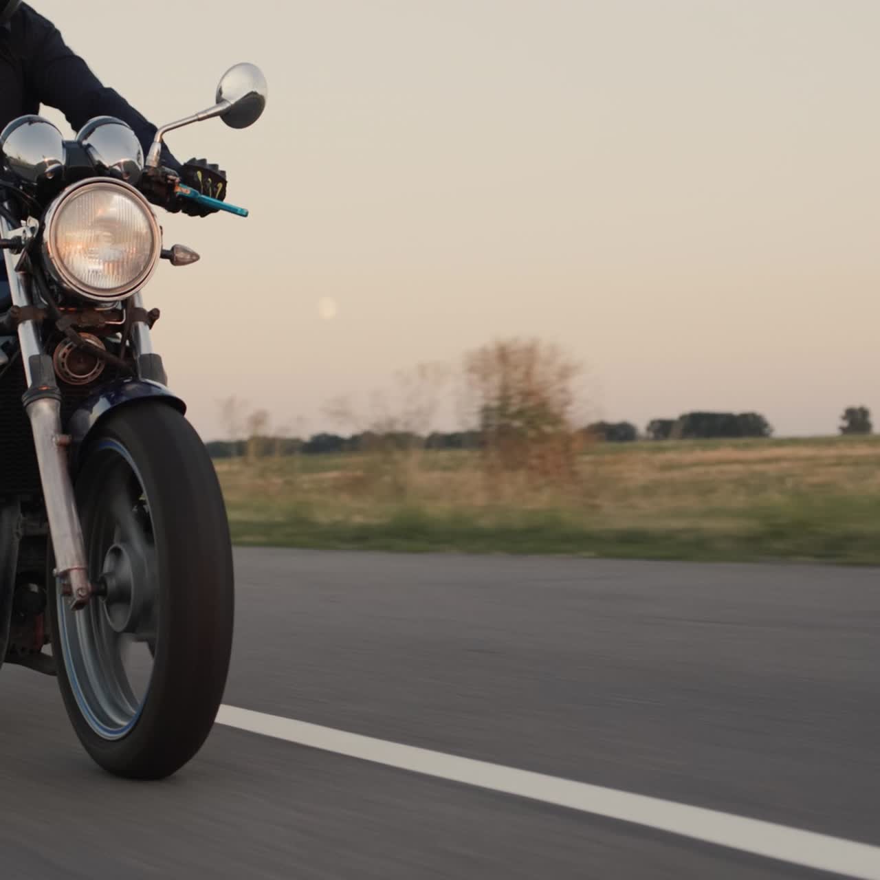Motociclista in abiti scuri percorre una strada rurale pittoresca