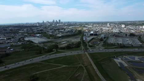 Aerial-drone-footage-showcasing-Calgary's-summer-scenery,-featuring-the-highway-and-industrial-area,-with-downtown-as-backdrop