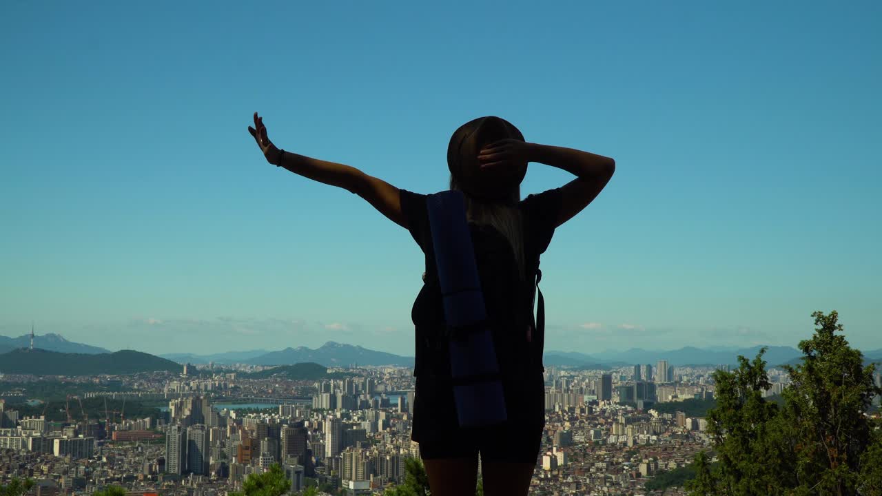 vista trasera de una mujer estirando los brazos en la cima de la montaña gwanaksan en corea del sur, con vistas al famoso distrito de seocho-gu - plano medio