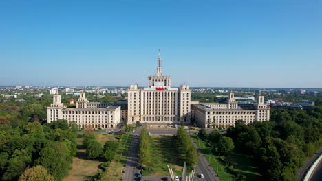 Revelación-Aérea-De-La-Casa-De-La-Plaza-De-La-Prensa-Libre-En-Bucarest,-Rumania,-Con-El-Imponente-Edificio-Casa-Presei-Al-Fondo,-Rodeado-De-Exuberante-Vegetación-Y-Altos-Edificios-De-Oficinas.