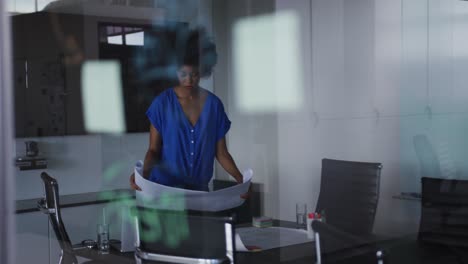 african american businesswoman unrolling technical drawing on table in meeting room