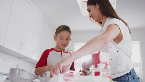 Pre-teen-Hispanic-boy-preparing-cake-mix-in-the-kitchen-with-his-mother,-close-up,-low-angle