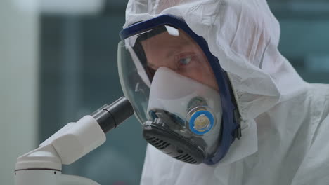 el hombre está usando un moderno microscopio electrónico para explorar bacterias y virus en el laboratorio protegiéndose con una máscara con respirador retrato de primer plano del científico