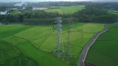 aerial orbit shot of high voltage transmission tower surrounded by rural plantations fields in indonesia