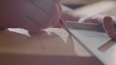hands of carpenter drawing line on wooden plank with pencil and set square