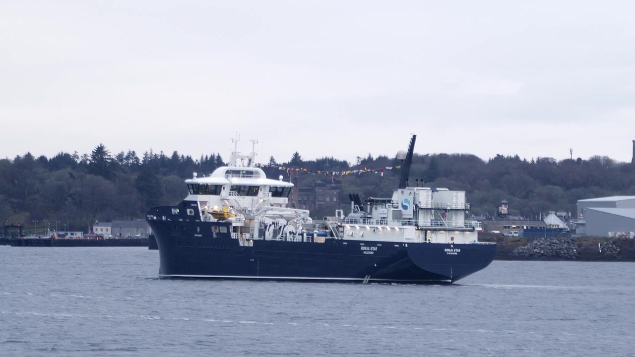 Tracking shot of a fish farming boat driving into harbour before anchoring. Shot near Stornoway on the Isle of Lewis, part of the Outer Hebrides of Scotland.