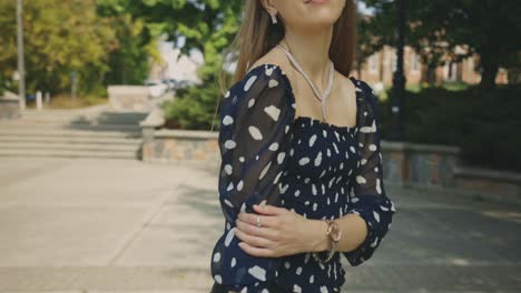 pretty blonde woman in casual outfit standing at the park with left hand holding her right arm posing in front of the camera - slow motion