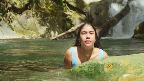 una mujer joven disfruta de un día soleado en una cascada en un bikini azul