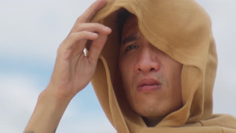 close up of a male chinese asiatic wearing a robe hood looking at the distance with a worried gaze during a wind storm