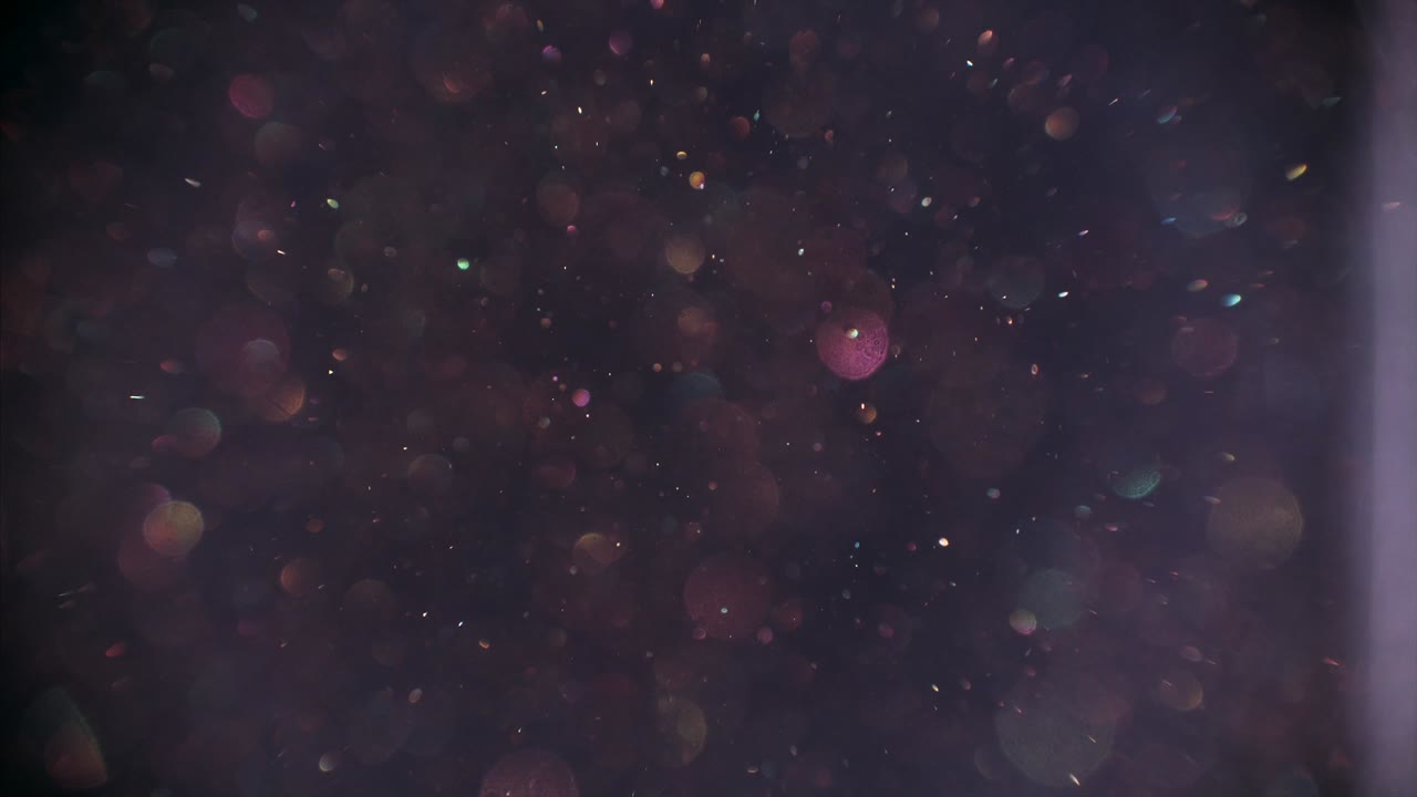 la polvere della natura si alza lentamente sullo sfondo grigio, bolle di bokeh sfocate luccicano in primo piano.