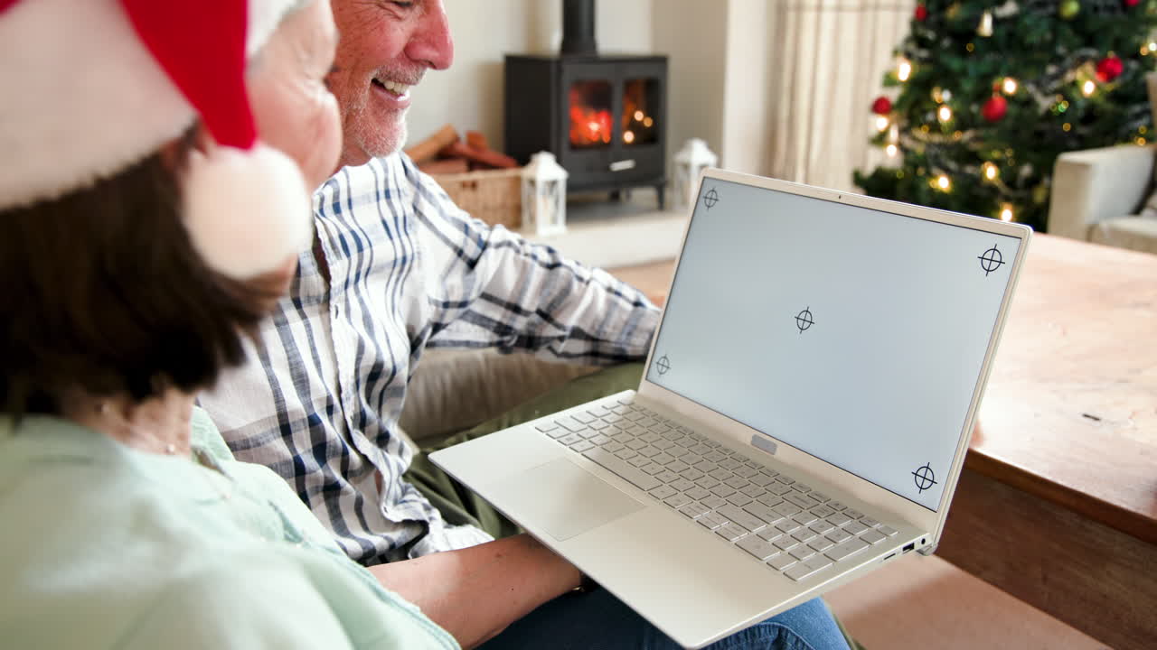 Senior couple video chatting on laptop by Christmas tree at home