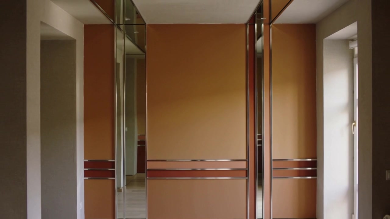 La telecamera si allontana rivelando un armadio a muro scorrevole in una stanza, mostrando un pannello a specchio.