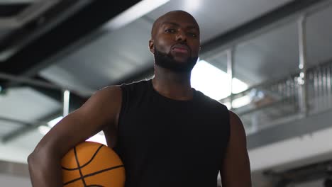 Portrait-Shot-Of-Male-Basketball-Player-On-Court-Holding-Ball-Under-Arm