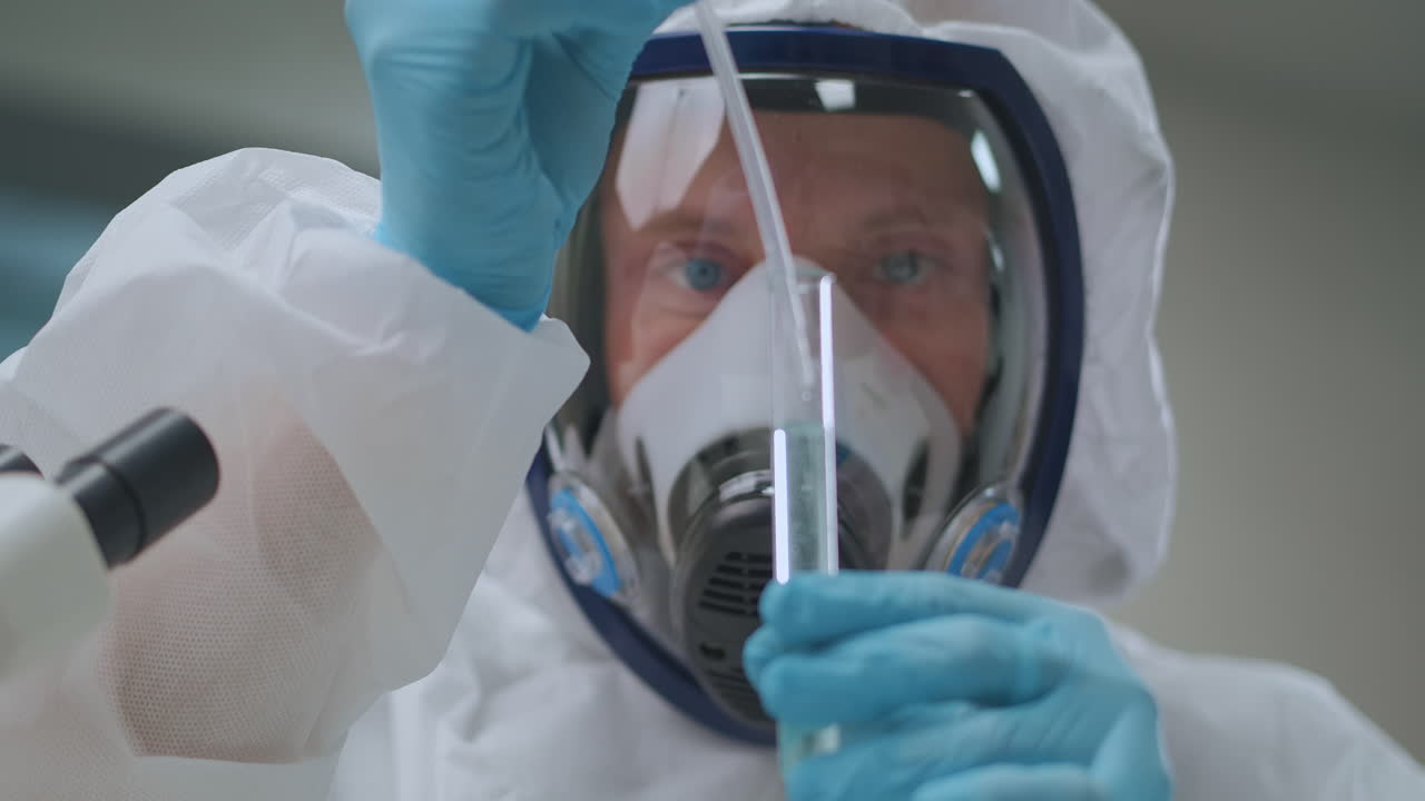 male chemist specialist dressed PPE suit is working with toxic chemicals in laboratory dropping reagent in tube dangerous chemical experiment