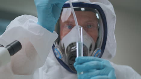 male-chemist-specialist-dressed-PPE-suit-is-working-with-toxic-chemicals-in-laboratory-dropping-reagent-in-tube-dangerous-chemical-experiment