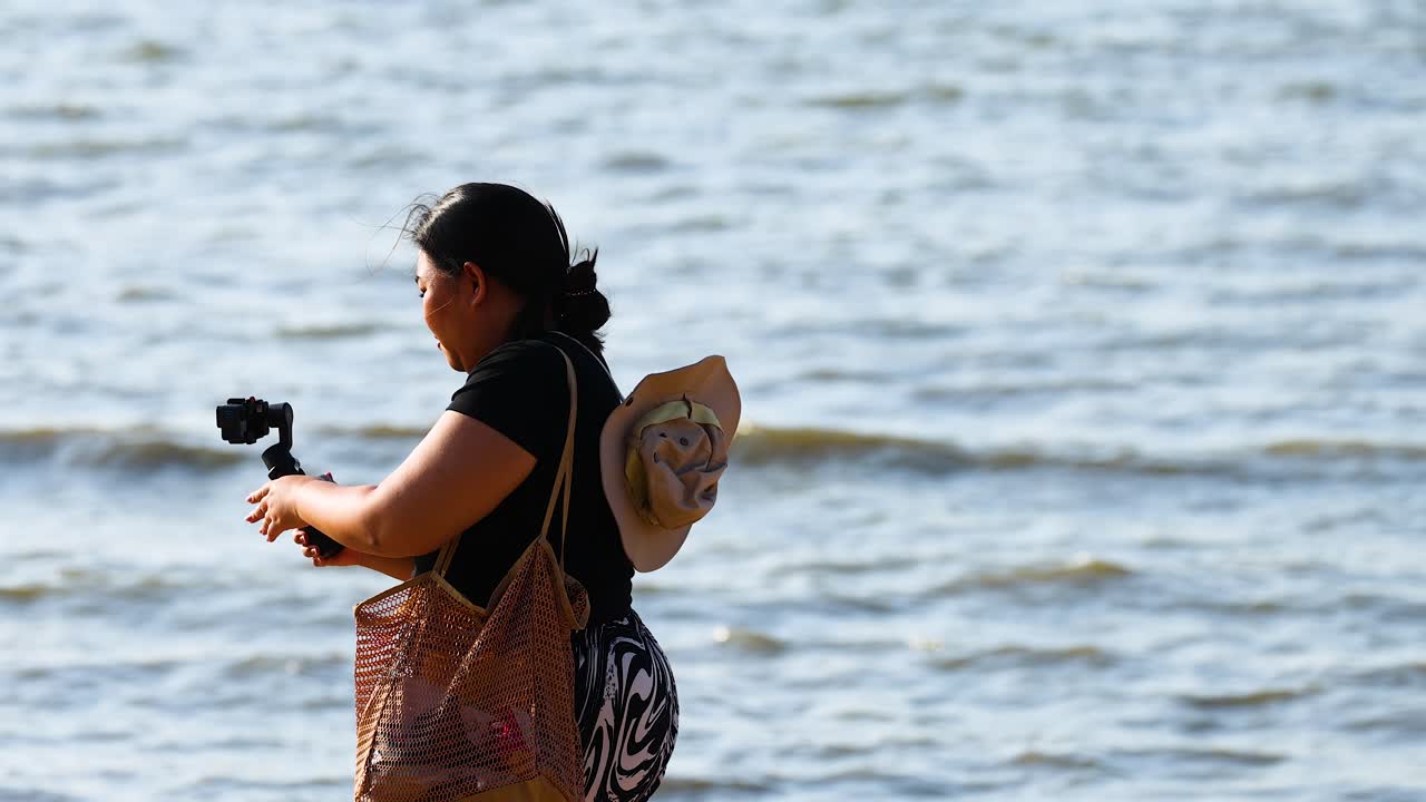 女性がビーチのボートの近くでビデオを録音する
