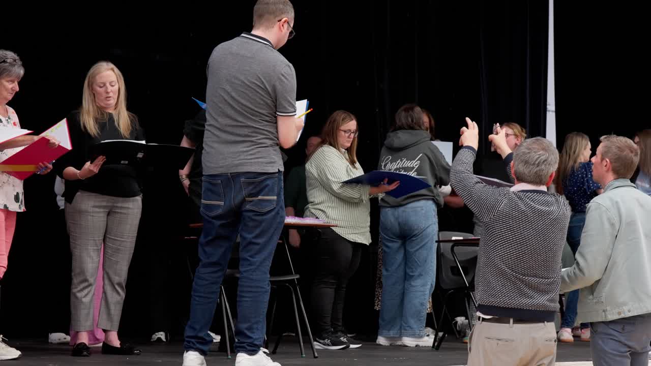 Group of amateur theatre actors rehearsing on stage with scripts, guided by a director. Creative community performance preparation on black stage with props