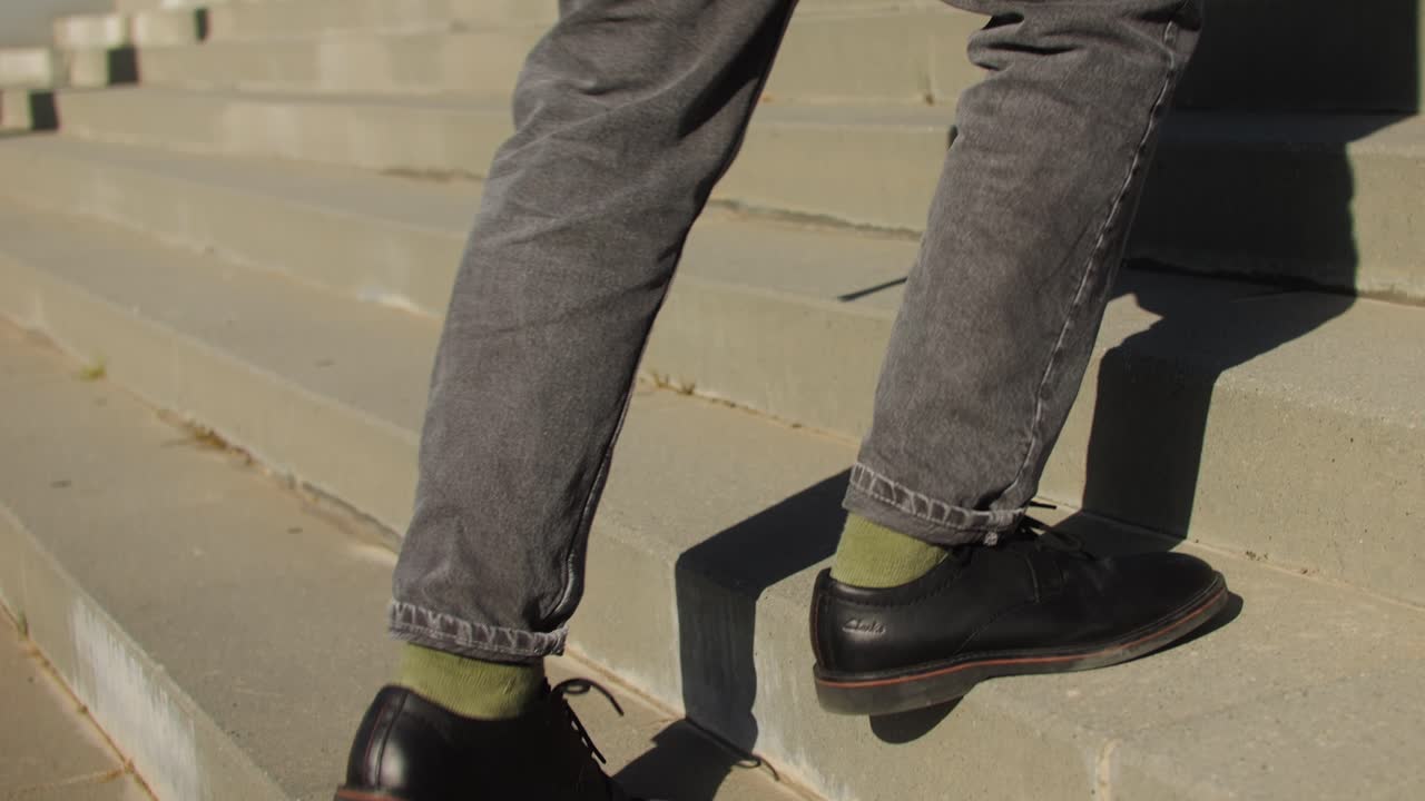 A man is climbing a set of stairs in the City, holding onto the handrail. The wind rustles his hair as he enjoys some leisurely recreation