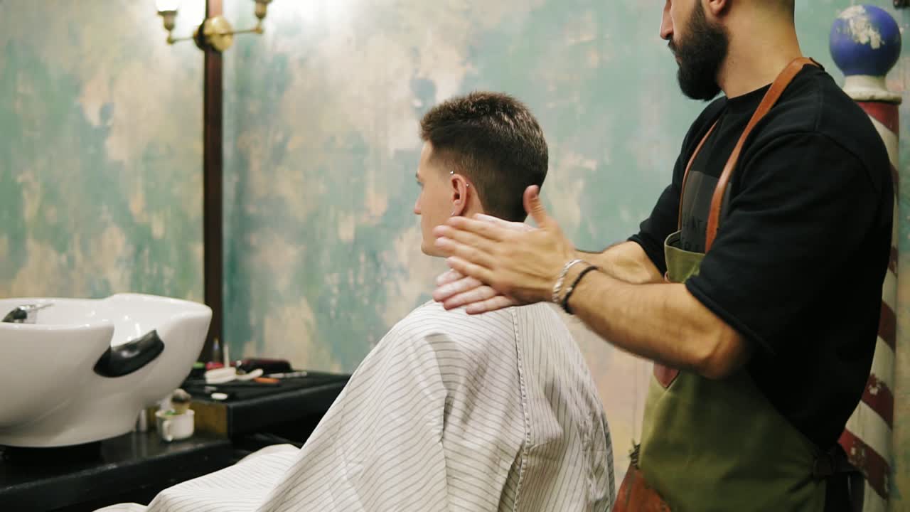 el peluquero barbudo está aplicando gel en el cabello de un elegante cliente masculino en un tiro de barbero. corte de pelo profesional para los jóvenes