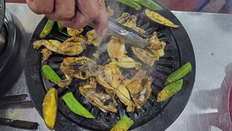 close-up frying chopped frog on small grill with okra plants at local da lat city restaurant, vietnam