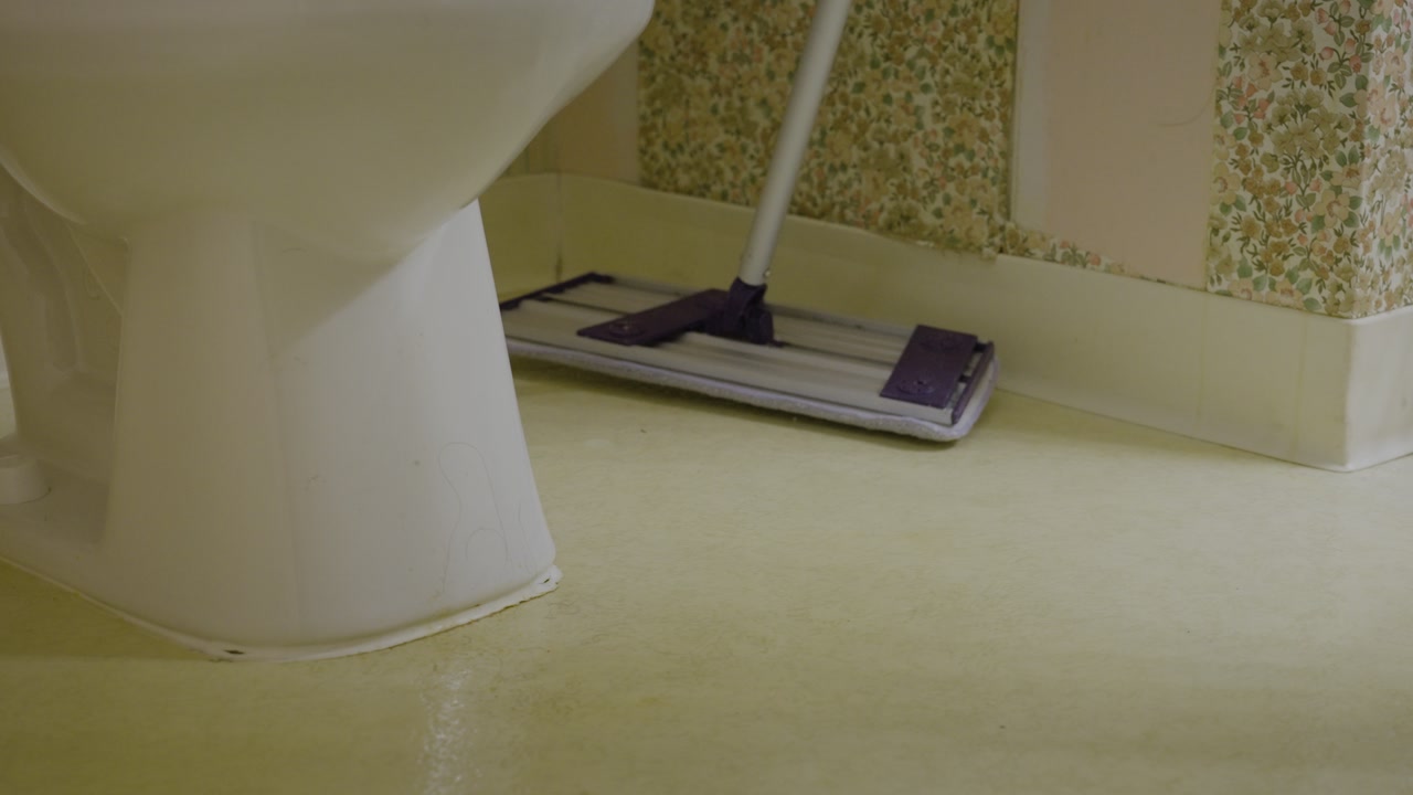 Dusting a bathroom floor before mopping.