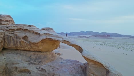 a tourist over natural arch of burdah rock bridge in wadi rum protected area in southern jordan, middle east