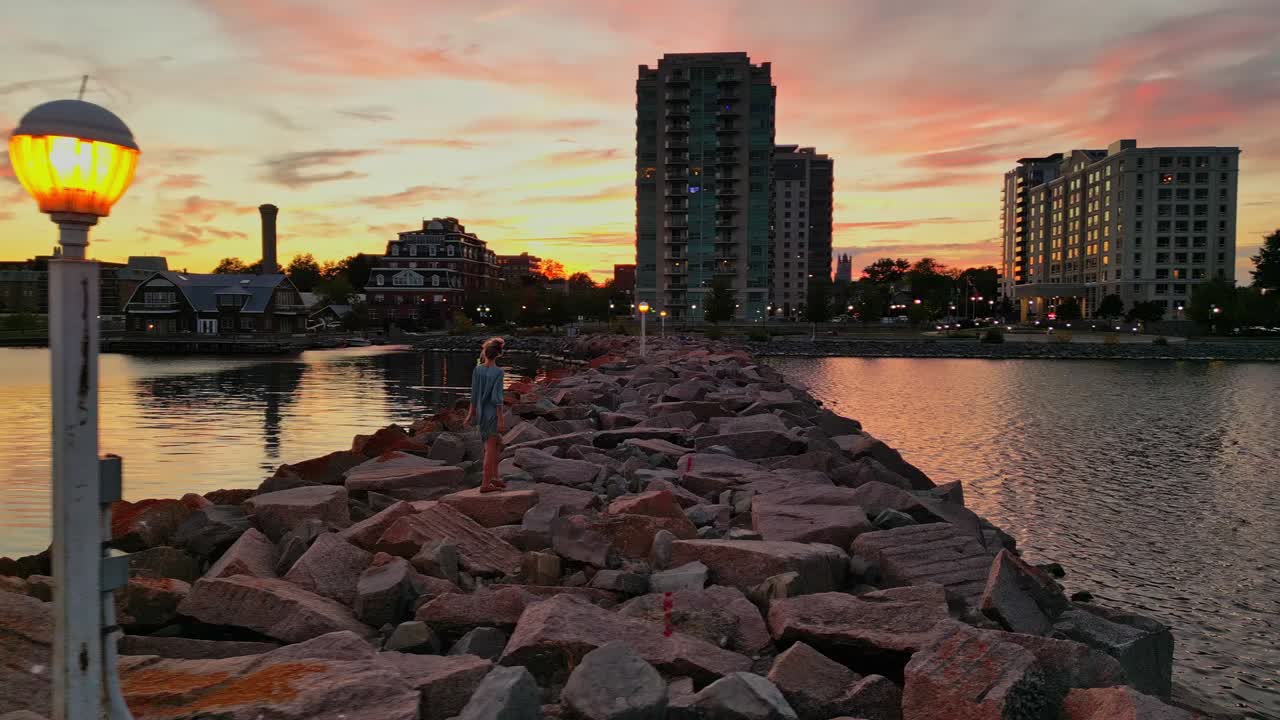해안가 공중 패닝 샷에서 일몰을 바라보는 젊은 여성