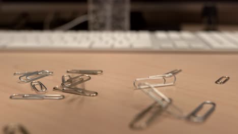 a hand full of paper clips slowly dropping onto an office desk a little bit at a time