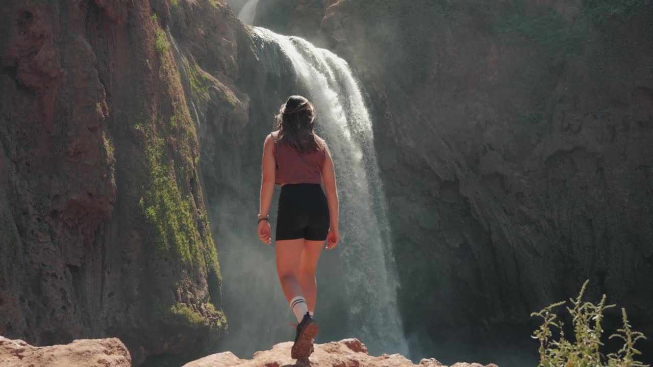 joven mujer caucásica caminando sobre rocas hacia las cascadas en ouzoud, marruecos