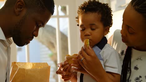 front view of young black mother feeding cupcake to her son in kitchen of comfortable home 4k