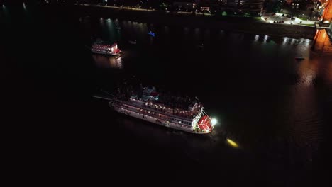 aerial view overlooking illuminated steamboats driving on the ohio river, nighttime in cincinnati, usa