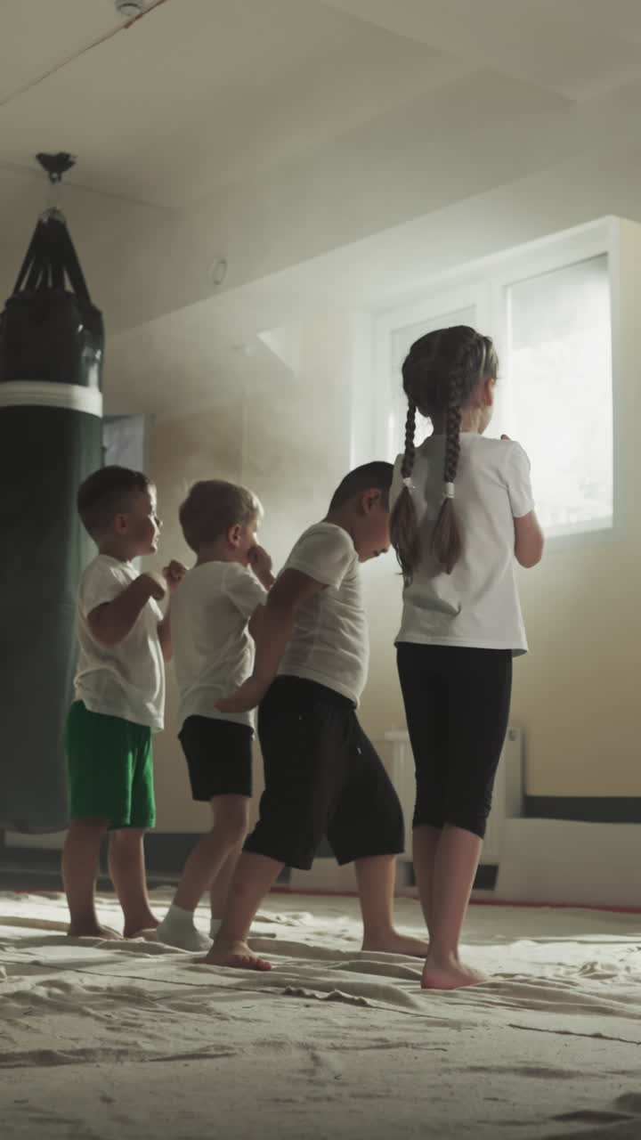 los niños golpean el aire con las manos imitando al entrenador en el gimnasio. niños pequeños activos entrenan el ataque con el maestro de artes marciales en la escuela de deportes en cámara lenta. vida saludable