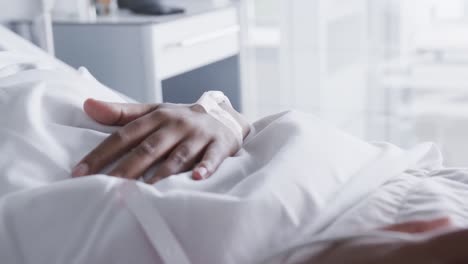 hands of african american female patient lying in bed in hospital room, slow motion