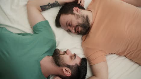 retrato de atractivos hombres gays barbudos parejas acostadas en la cama juntos, hablando y acariciándose unos a otros